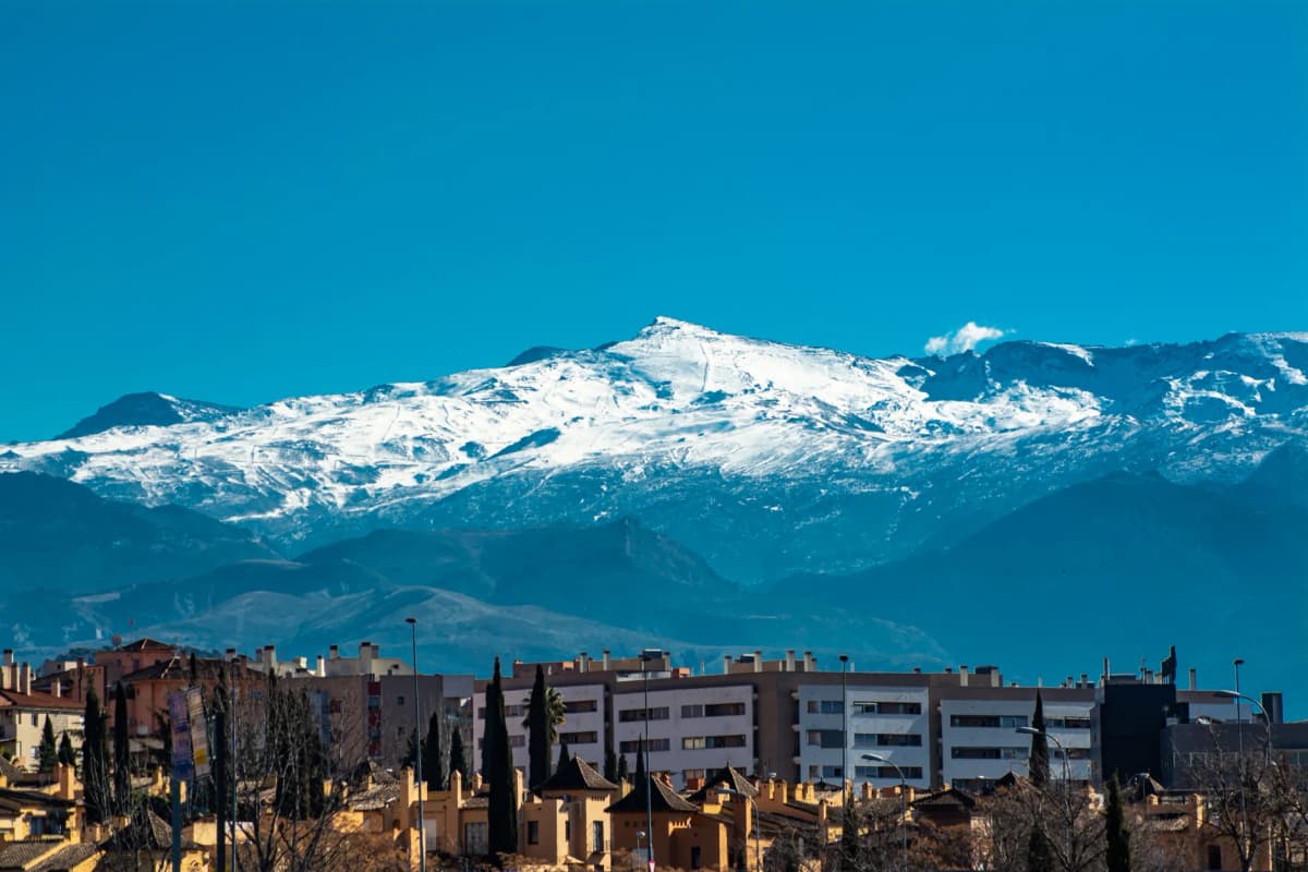 Panoramic view of snowy Sierra Nevada mountains towering over Granada's urban landscape.