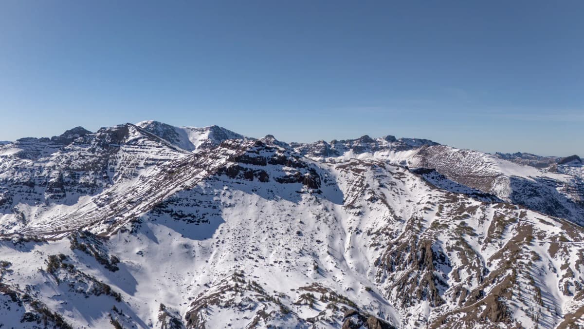 Breathtaking aerial photograph capturing the snow-covered Sierra Nevada mountains under a clear blue sky.